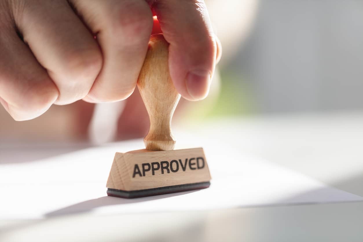An image of someone stamping a paper with a stamp that reads “Approved”.