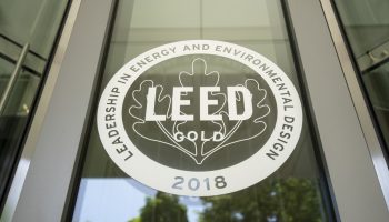 LEED Gold Certification Seal Displayed On Glass Entrance Door, Representing Sustainable Commercial Construction Practices And Energy-efficient Building Standards.