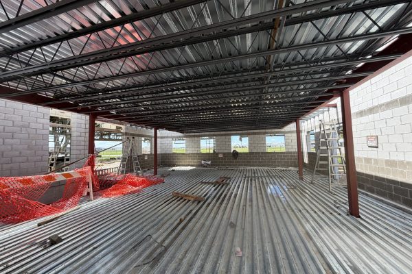 Interior of a commercial building under construction with steel framing, metal decking, and concrete block walls.