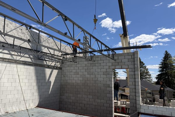 Steel roof trusses being installed on a commercial masonry building using a crane during construction.