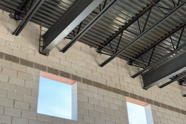 Interior of a commercial building under construction with exposed steel beams, metal roof deck, and concrete block walls.