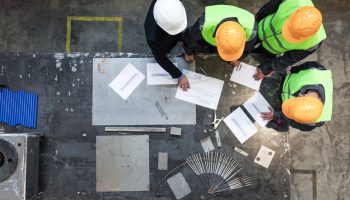 A Small Team Of Architects And Engineers Looking Over Some Blueprints, With A Laptop Nearby.