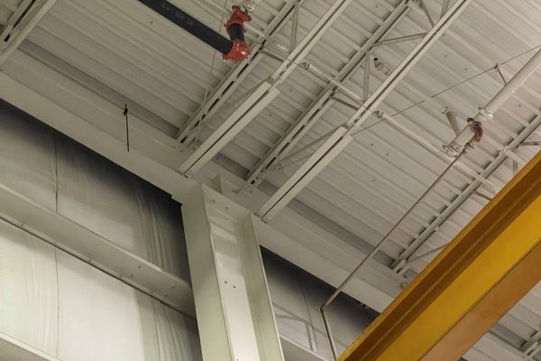 Industrial facility interior with structural steel framing, overhead crane beam, and insulated metal roof system.