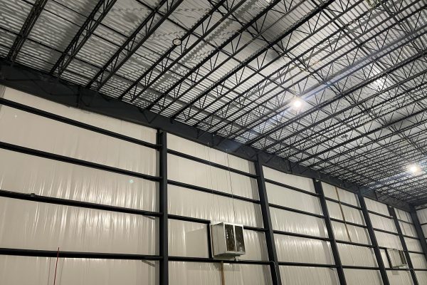 Interior of a pre-engineered metal building under construction with exposed steel framing and insulated wall panels.