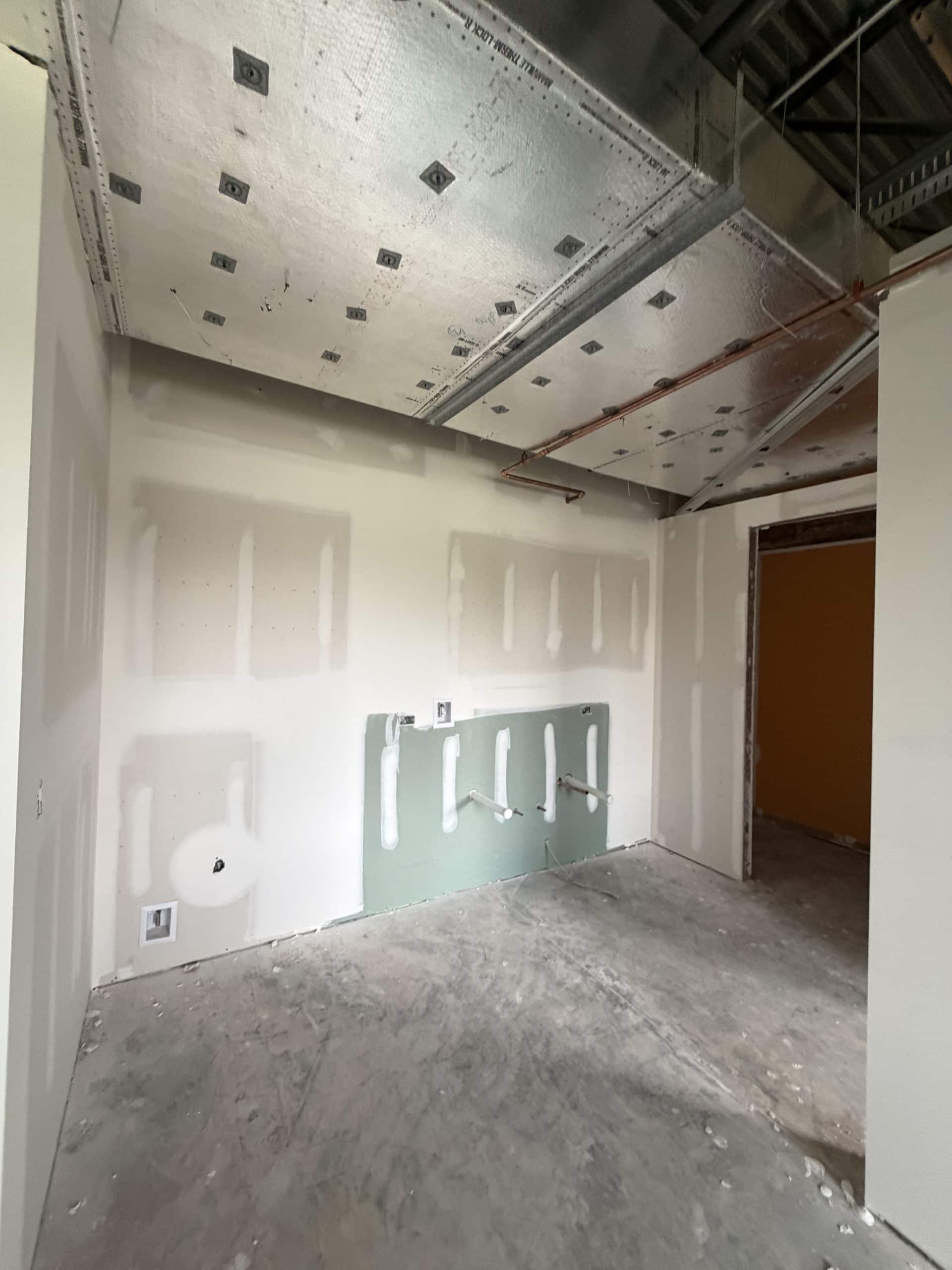 Commercial interior build-out with insulated HVAC ductwork, unfinished drywall, and utility rough-ins during construction.