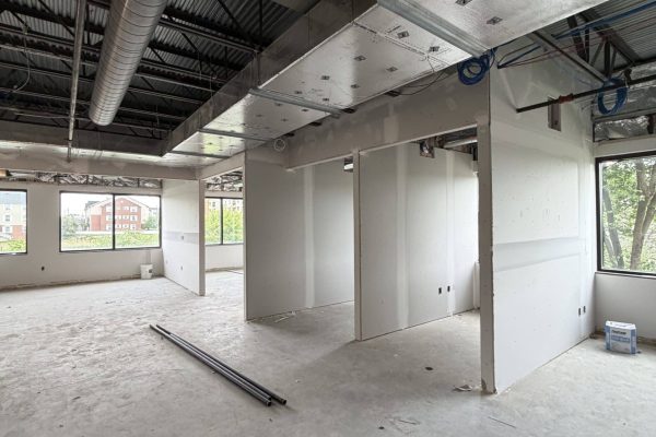 Commercial office interior under construction with HVAC ductwork, exposed steel framing, and newly installed drywall partitions.