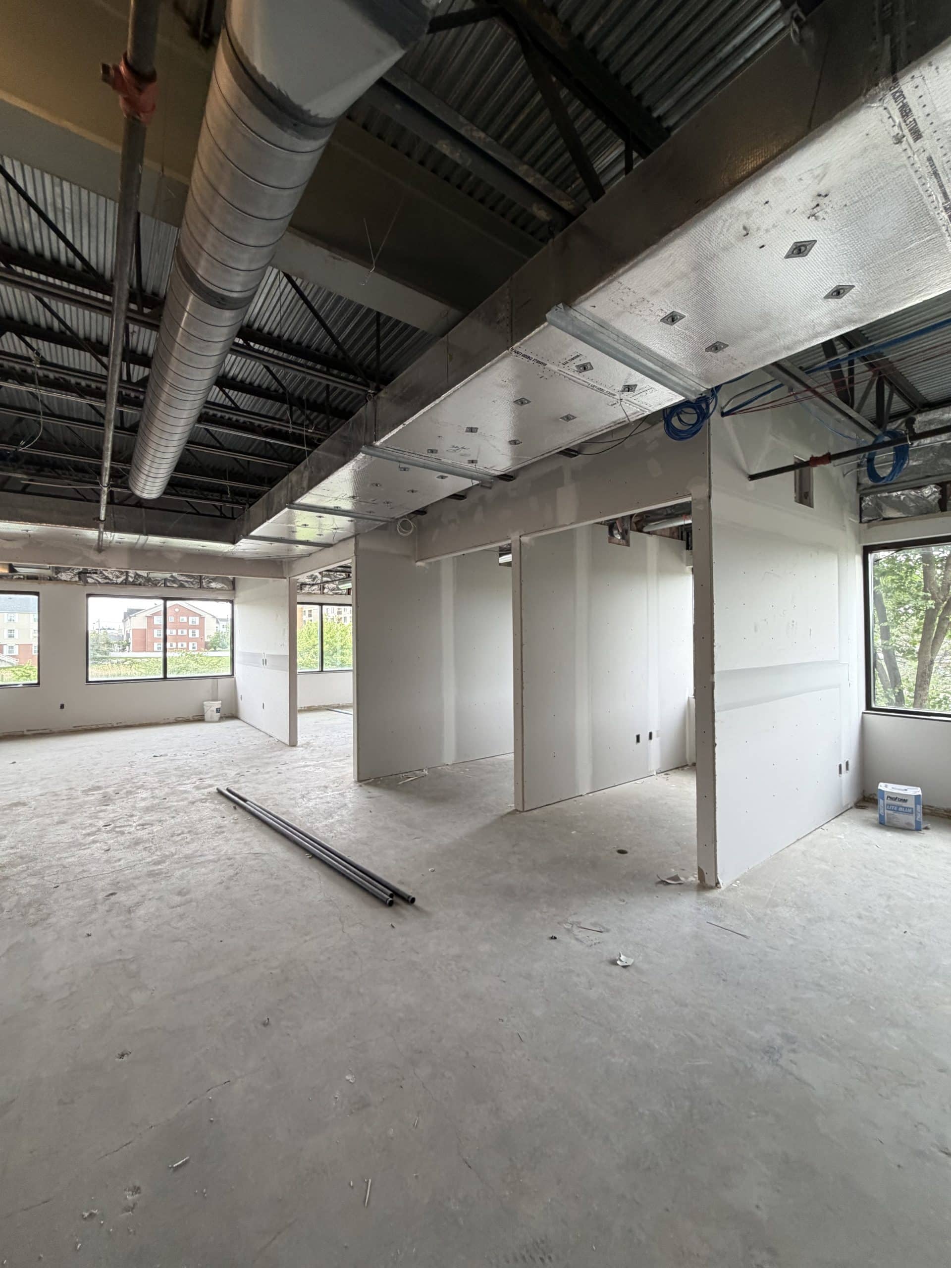 Commercial office interior under construction with HVAC ductwork, exposed steel framing, and newly installed drywall partitions.